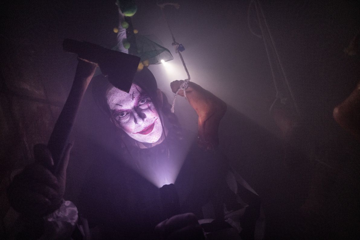 Creepy clown standing in the darkness with a torch illuminating their smile.
